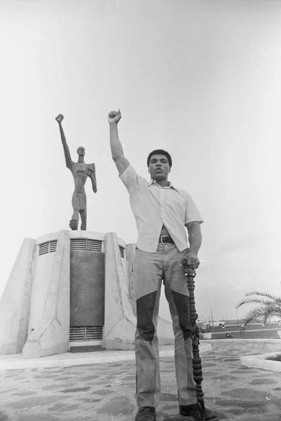 Kids Sports Art: Muhammad Ali Posing In Front Of The Le Militant Statue, Kinshasa, Zaire by Muhammad Ali Enterprises