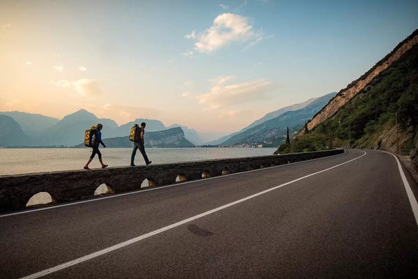 Alex Buisse: Two Climbers Walk Home Next To A Road And Lago di Gardo, Arco, Trentino, Italy by Alex Buisse