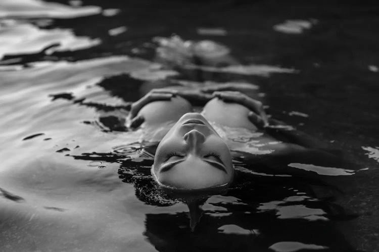 Black And White Photo Of Woman Posing With Closed Eyes While Lying In The Water