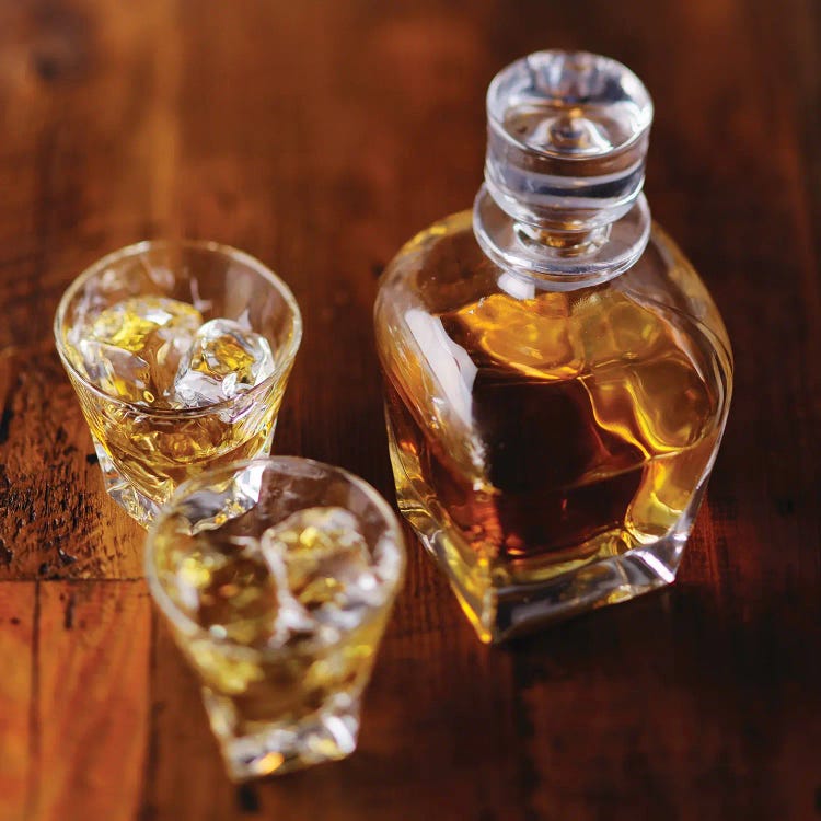 A Whiskey Bottle And Two Glasses Of Scotch On The Rocks On A Wooden Table