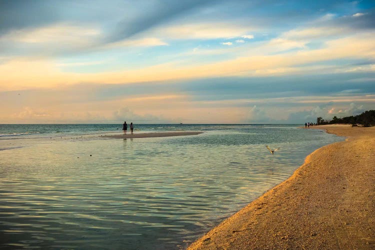 People standing on a sandbar in the water watching sunset