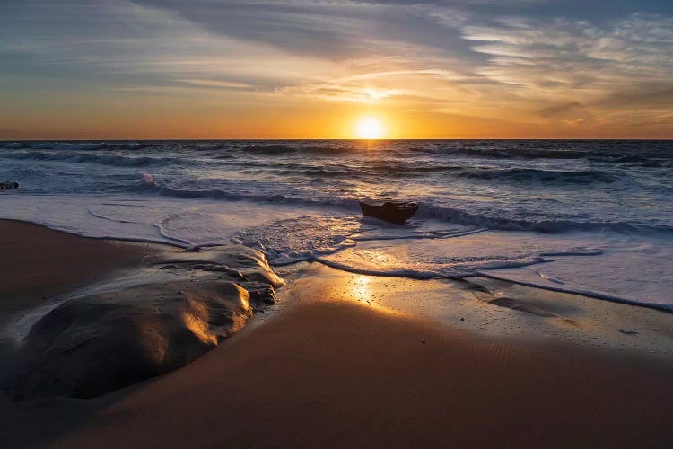 Sunset reflecting off the water on the sand of a beach