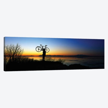 Silhouetted cyclist holding bicycle over head, river's edge, sunset, Alaska. Canvas Print #PIM12465} by Panoramic Images Canvas Artwork