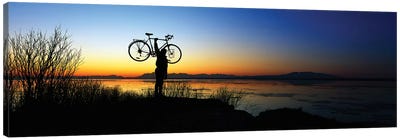 Silhouetted cyclist holding bicycle over head, river's edge, sunset, Alaska. Canvas Art Print - Alaska Art