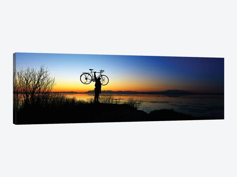 Silhouetted cyclist holding bicycle over head, river's edge, sunset, Alaska. by Panoramic Images 1-piece Canvas Art