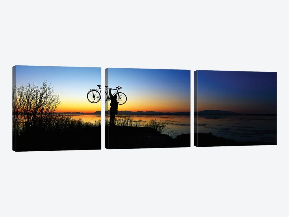 Silhouetted cyclist holding bicycle over head, river's edge, sunset, Alaska. by Panoramic Images 3-piece Canvas Wall Art