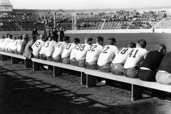 1940s High School Or Collegiate Football Teams From Behind All Sitting On Sideline Benches