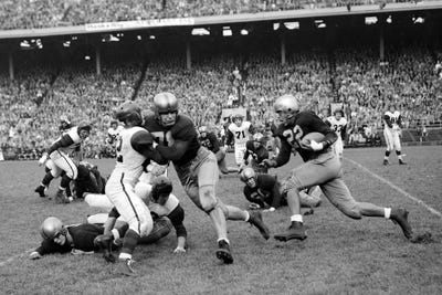Canvas Print: 1950s College Football Game Showing Blockers Making Tackles For Running Back With Capacity Crowd In Stands In Background by Panoramic Images - thumbnail