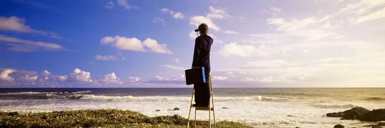 Businessman On A Ladder Looking Through Binoculars On A Beach, California, USA