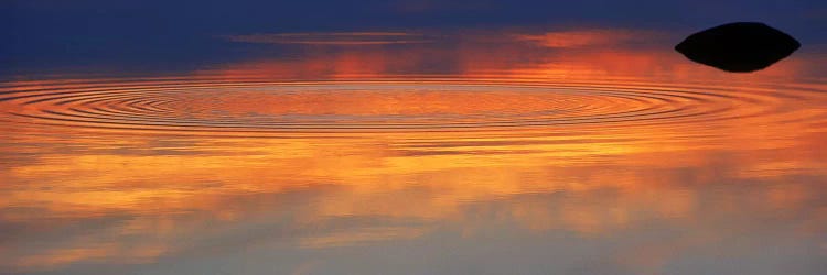 Reflection of clouds with circular ripples spreading outward across glassy lake waters at sunset