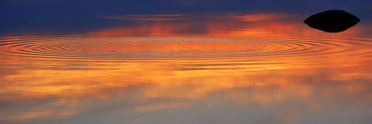 Reflection of clouds with circular ripples spreading outward across glassy lake waters at sunset by Panoramic Images wall art