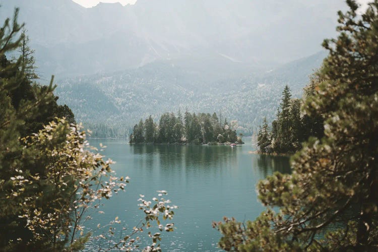 Forest Island In A Mountain Lake Framed By Trees On A Sunny And Hazy Day