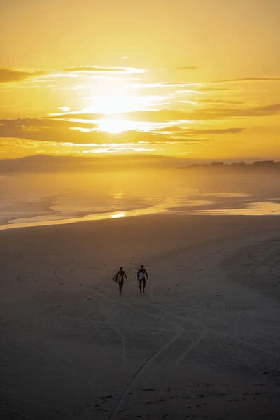 Two Surfers Walking On Shoreline At Sunset