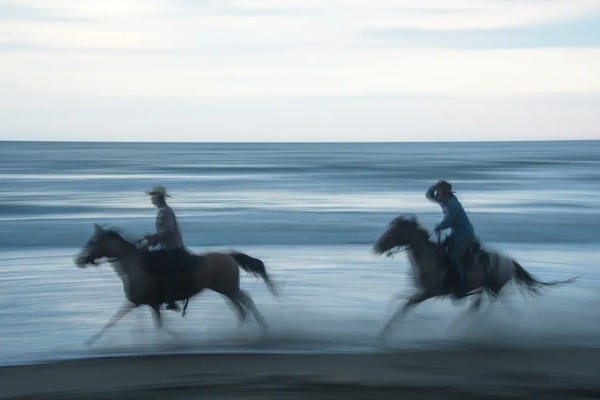 Joel Sartore: Two Cowboys Ride Horses Through The Waves On Virginia Beach, Virginia by Joel Sartore