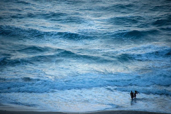 Joel Sartore: A Couple Plays In The Ocean Waves At Dusk At Riviera Beach by Joel Sartore