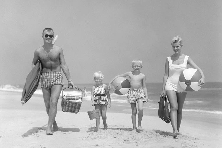 1950s Family Of Four Walking Towards Camera With Beach Balls Umbrella Picnic Basket And Sand Bucket