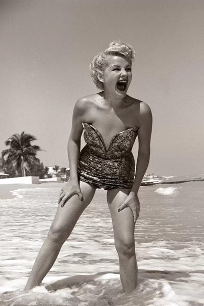 Fashion Photography: 1950s Laughing Blonde Woman In Strapless Low Cut Bathing Suit Swim Wear Wading Up To Ankles In Surf by Vintage Images
