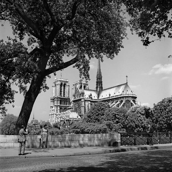 Notre Dame Cathedral: 1950s Paris France Tourist Couple Man With Camera Photographing Woman Notre Dame Cathedral In Background by Vintage Images