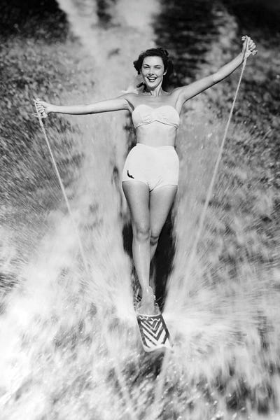 Fashion Photography: 1950s Smiling Woman In White Two Piece Bathing Suit Aquaplaning Water Skiing Looking At Camera by Vintage Images