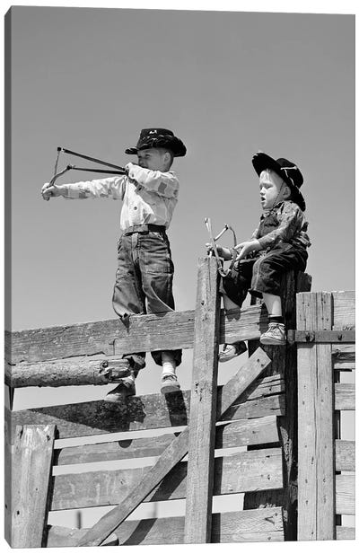 1950s Two Young Boys Dressed As Cowboys Shooting Slingshots On Top Of Wooden Fence Outdoor Canvas Art Print - Cowboy & Cowgirl Art