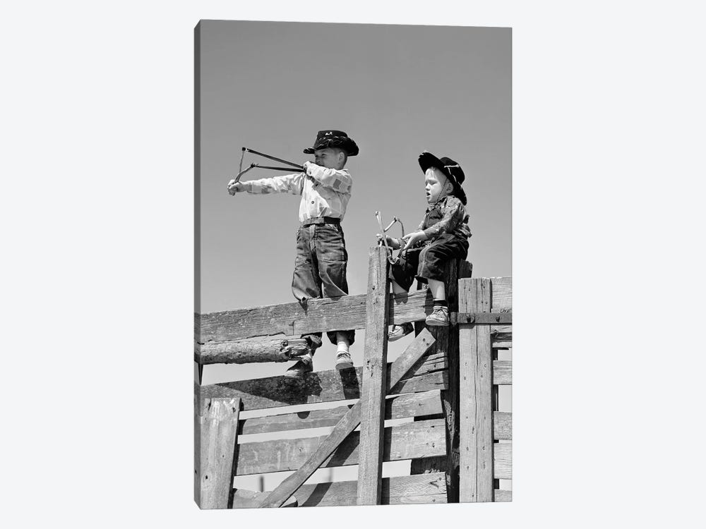 1950s Two Young Boys Dressed As Cowboys Shooting Slingshots On Top Of Wooden Fence Outdoor by Vintage Images 1-piece Art Print