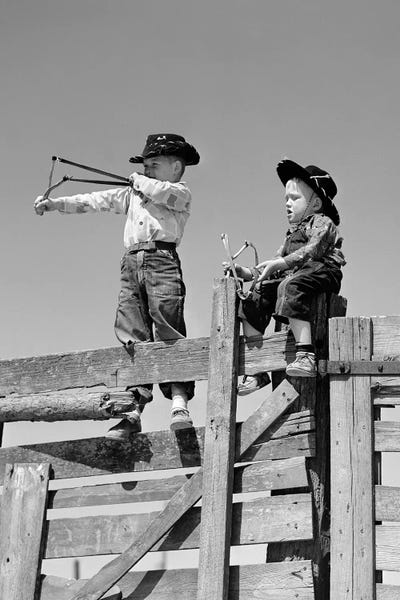 Costumes: 1950s Two Young Boys Dressed As Cowboys Shooting Slingshots On Top Of Wooden Fence Outdoor by Vintage Images