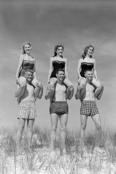 Groups: 1950s-1960s Three Couples At Beach On Dunes With Women In Identical Bathing Suits Sitting On Men's Shoulders by Vintage Images