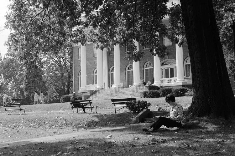 1960s Anonymous Silhouetted Female College Student Sitting Under Tree Studying With Campus Building In Background by Vintage Images wall art