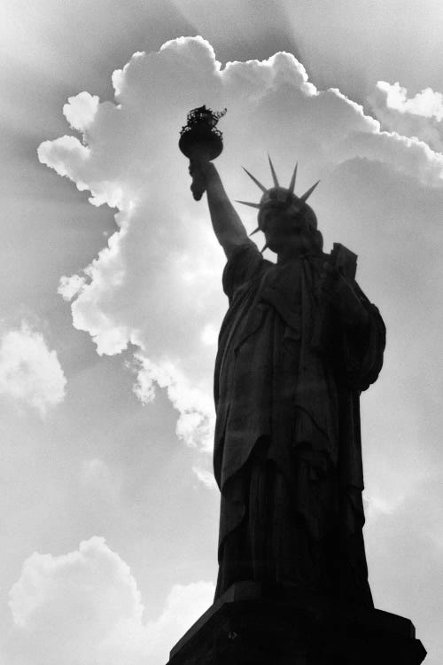 1960s Silhouette Of Statue Of Liberty With Sun Ray Clouds Behind