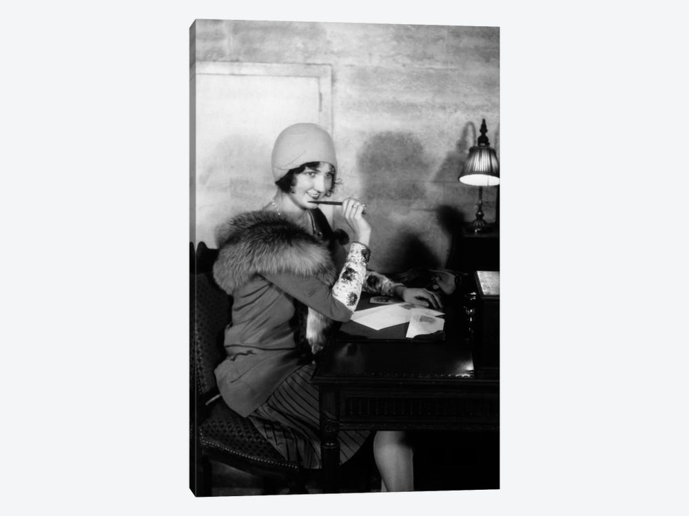 1920s Smiling Woman With Pen To Lips Wearing Cloche Hat And Fur Collar Coat Writing A Letter At Hotel Lobby Desk With Lamp by Vintage Images 1-piece Canvas Print