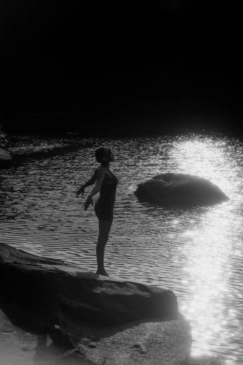 1920s Sunset Silhouette Of Anonymous Woman Standing On A Rock Near Water About To Dive In