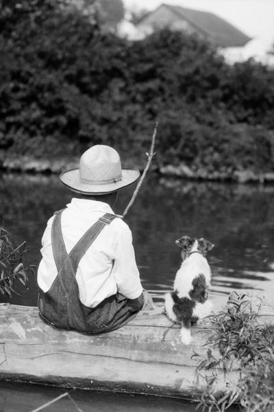 Puppies: 1920s-1930s Farm Boy Wearing Straw Hat And Overalls Sitting On Log With Spotted Dog Fishing In Pond by Vintage Images