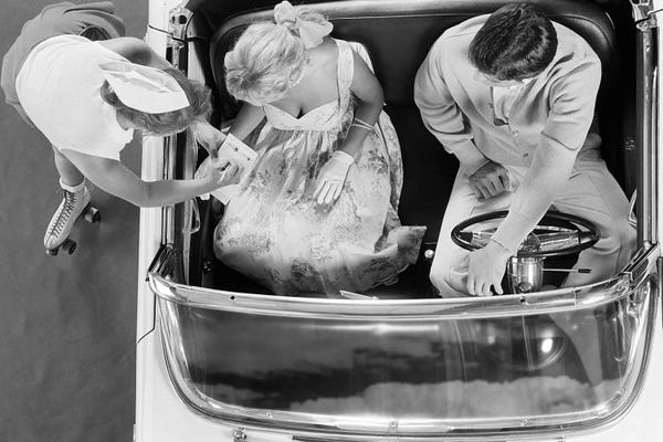 Figurative Photography: 1950s 1960s Aerial View Of Carhop On Roller Skates Taking Order From Couple In Convertible Automobile by Vintage Images