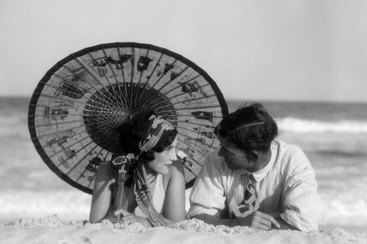 1920s Romantic Couple Man Woman Looking At One Another Lying Face To Face Under Oriental Parasol On Sandy Beach