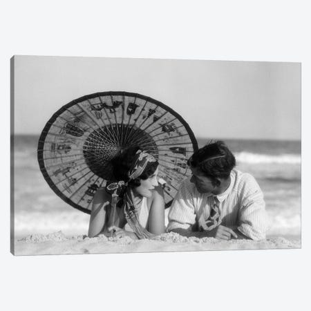 1920s Romantic Couple Man Woman Looking At One Another Lying Face To Face Under Oriental Parasol On Sandy Beach Canvas Print #VTG676} by Vintage Images Canvas Artwork