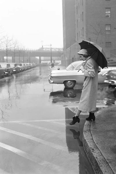 Vintage Images: 1950s Woman In Rain Coat Hat Boots Holding Umbrella Crossing City Street In Wet Foul Weather by Vintage Images