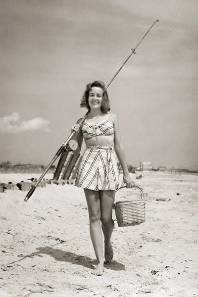 1940s Smiling Young Woman Walking On Beach Looking At Camera Wearing Two Piece Bathing Suit Skirt Carrying Surf Fishing Gear by Vintage Images canvas print
