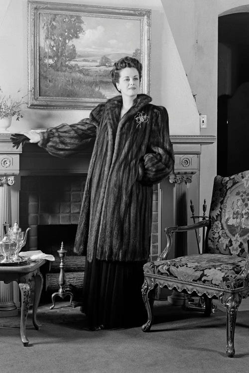 1940s Woman In Formal Living Room Standing In Front Of Fireplace Wearing Full-Length Fur Looking At Camera