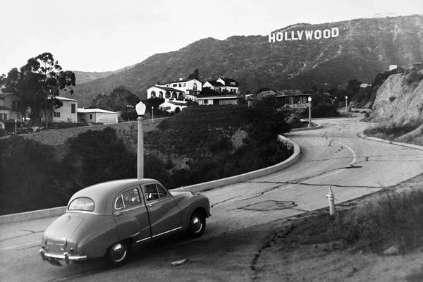 Signs: 1950s Austin Car Driving Up The Hollywood Hills With Hollywood Sign In Distance Los Angeles Ca USA by Vintage Images