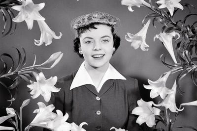 1950s Portrait Smiling Brunette Woman Wearing Easter Bonnet Hat Looking At Camera Surrounded Framed By Easter Lilies by Vintage Images art print