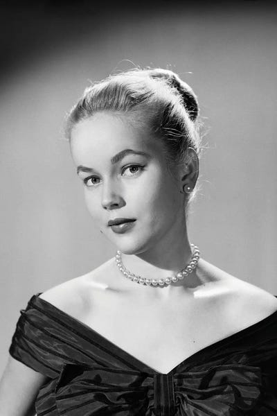 Historical Fashion: 1950s Portrait Young Blond Woman Serious Facial Expression Pearl Necklace Black Satin V Neckline Evening Dress Looking At Camera by Vintage Images