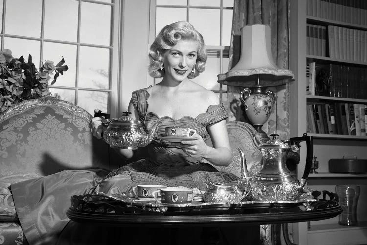 1950s Smiling Blond Woman Elegant Dress & Home Furnishings Pouring Cup Tea From Silver Service Sitting Couch Looking At Camera