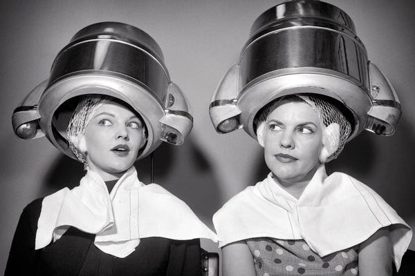 Historical Fashion: 1950s Two Women Sitting Under Beauty Salon Hair Dryers Wearing Hairnets Towels Talking Gossip by Vintage Images