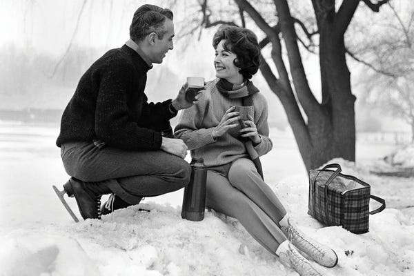 Historical Fashion: 1960s Smiling Couple In Snow Wearing Ice Skates Drinking Hot Beverage From Thermos by Vintage Images
